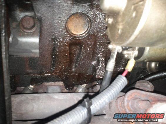 Close-up of an oily engine block with a starter motor and wiring attached
