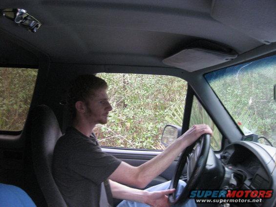 Interior view of a man driving a vehicle, with trees and brush visible through the windows