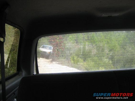 White SUV driving on a dirt road through trees, seen from inside another vehicle