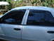 2002 Ford Crown Victoria - The side profile of a white sedan shows tinted windows and black door handles against a backdrop of greenery and a fence.