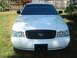 2002 Ford Crown Victoria - White 2002 Ford Crown Victoria parked in a grassy area with a wooden fence in the background.