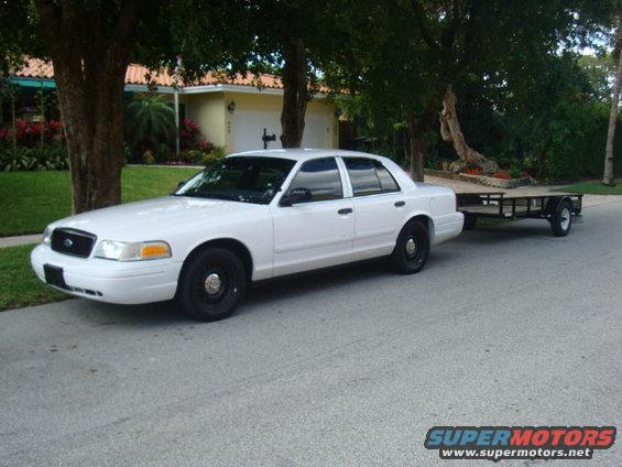 2002 Ford Crown Victoria sedan with black steel wheels, towing a small utility trailer