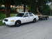 2002 Ford Crown Victoria - White 2002 Ford Crown Victoria sedan is parked on a residential street, towing a trailer.