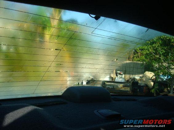 View through a rear window with defroster lines, showing trees and some clutter outside