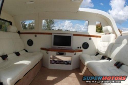 Limousine interior showing white leather seats, a TV, and speakers