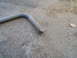 1979 Ford Bronco - A rusted metal pipe with a mounting bracket lies on an asphalt surface.