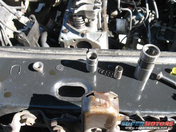 Engine lifters and springs on a black metal surface with engine components in the background