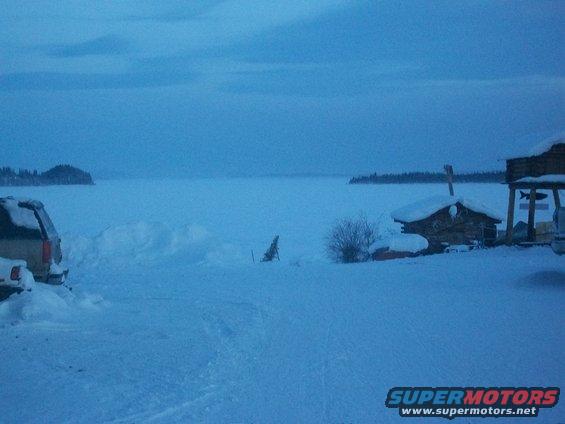 Side view of a tan SUV partially buried in snow next to a frozen lake