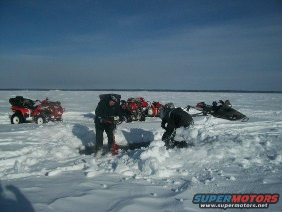 People ice fishing on a frozen body of water with ATVs and snowmobiles nearby