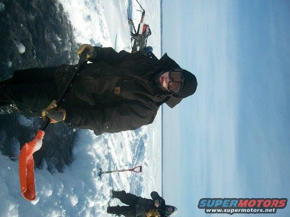 Two people in winter gear on a frozen surface with snowmobiles in the background