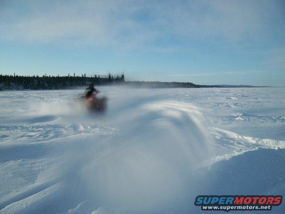 Snowmobile moving across a snowy landscape, kicking up a spray of snow