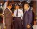 2003 Ford Crown Victoria - Three men, two in suits and one in a military uniform, converse outdoors near a flag.