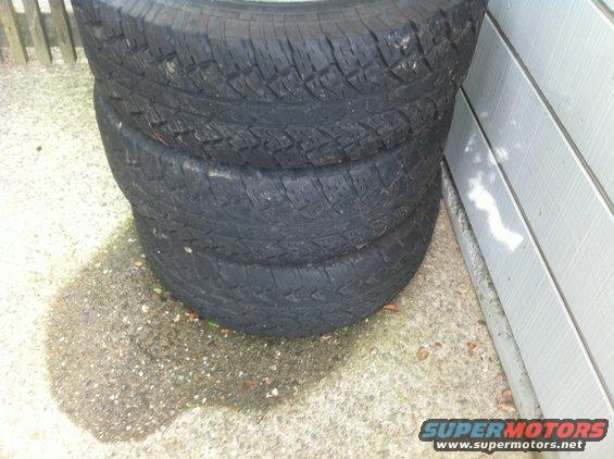 Stack of four black tires leaning against a white wall
