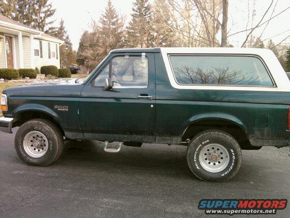 Green 1993 Ford Bronco side view, white top, silver wheels, on asphalt