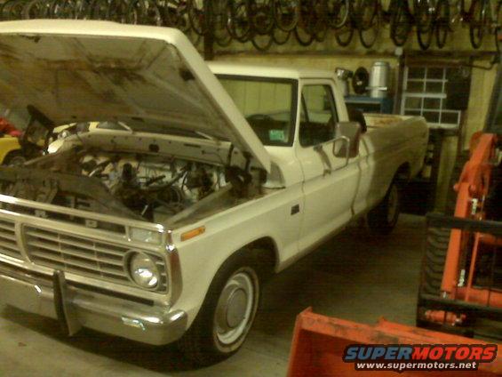White 1973 Ford F-100 pickup truck with hood open, showing engine bay. Parked indoors