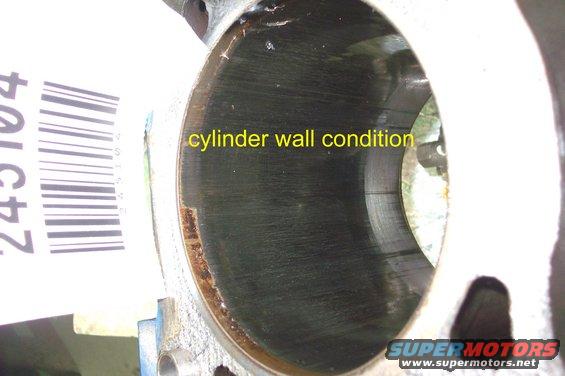 Engine cylinder wall with visible scoring and rust marks, next to a barcode sticker