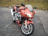 Orange sportbike motorcycle parked on asphalt with dry grass in background