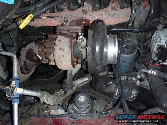 Engine bay with turbocharger, exhaust manifold, and oil filter visible. Yellow 'TRANS FLUID' dipstick is also in view