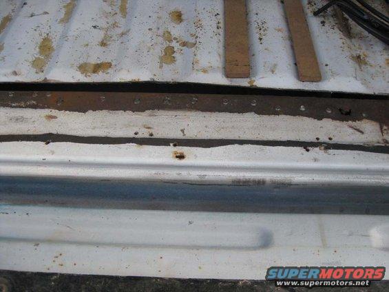 rusted metal strip with rivets on a white surface, possibly a truck bed or tailgate