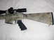 1991 Ford Bronco - A rifle with a camouflage pattern and a mounted scope is shown against a white background.