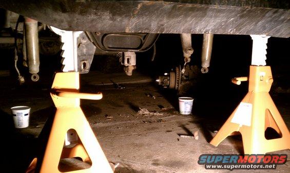 Vehicle undercarriage supported by jack stands, showing suspension components and brake assembly