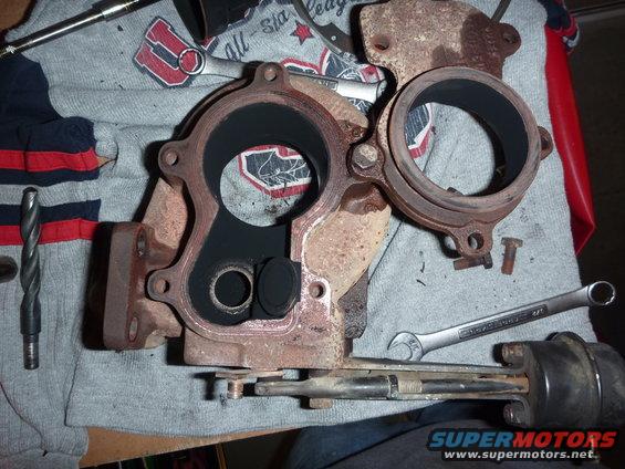 Rusty turbocharger assembly with black soot inside, resting on a grey cloth with red and blue stripes. Tools are visible