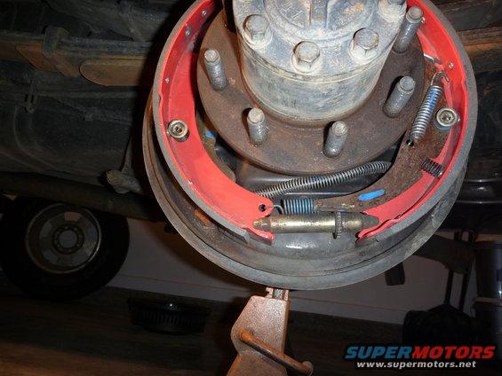 Close-up of a vehicle's rear brake drum assembly with new red brake shoes and springs