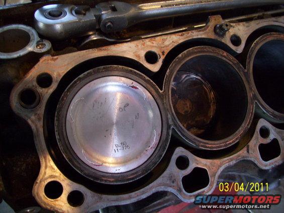 Engine block with two pistons visible, one with markings '0.50 11-775'. A ratchet is on top