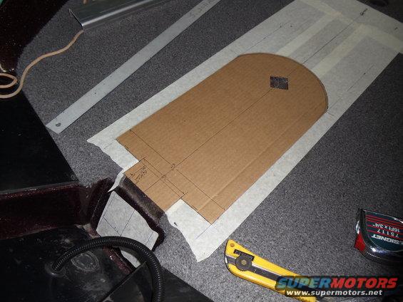 Cardboard template with measurements taped to carpet, next to a utility knife and tape measure