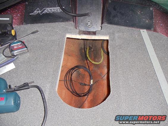 Boat interior with gray carpet and an open access hatch revealing wiring and a rope