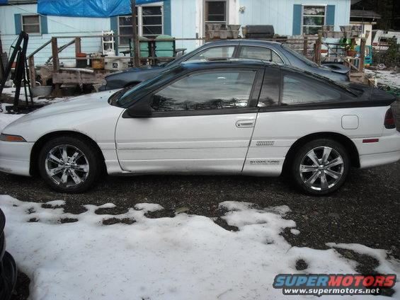 Side view of a white coupe with a black roof and chrome wheels, showing '16V DOHC TURBO' badging