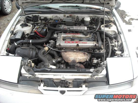 Engine bay of a white 1990s Mitsubishi Eclipse with a DOHC 16-valve engine visible