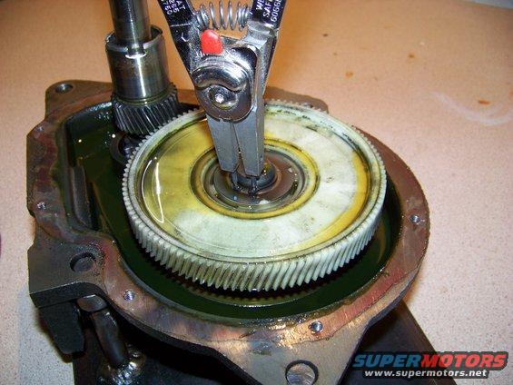 Transmission gear assembly with snap ring pliers removing a ring from a white plastic gear submerged in oil