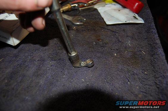 Close-up of a metal tool with a socket end, held by a hand, on a dark cloth surface