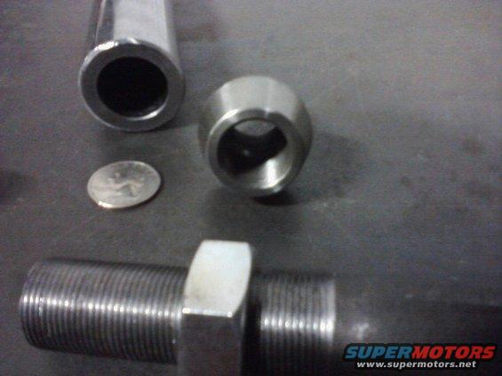 Metal rod with threaded end and nut, two other metal parts, and a coin on a dark surface