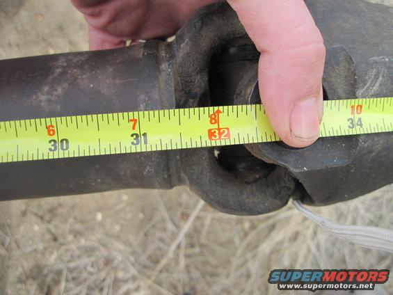 Measuring a driveshaft with a yellow tape measure. The tape shows about 32 inches