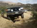 1978 Ford Bronco - A black Ford Bronco tackles a challenging off-road path, with another white SUV visible in the background.