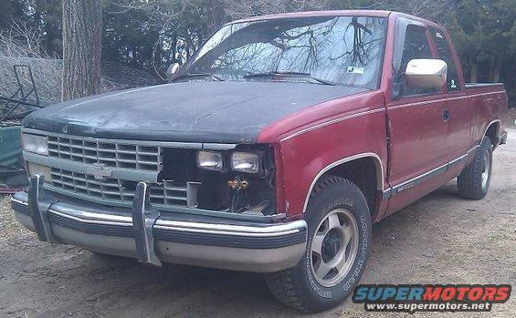 Red pickup truck, hood is a different color, missing headlight and grille section