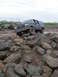 1991 Ford Bronco - A dark blue Ford F-Series truck attempts to traverse a challenging rocky and muddy obstacle course.