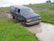 1991 Ford Bronco - This dark blue pickup truck navigates a muddy path, its front end submerged in water.