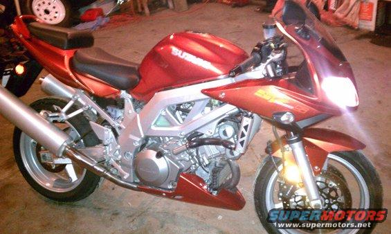 Red 2003 Suzuki SV1000S motorcycle parked indoors. Visible 'SUZUKI' on tank and 'SV1000S' on fairing