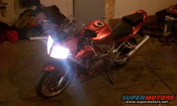 Red 2003 Suzuki SV1000S motorcycle with headlights on, parked indoors