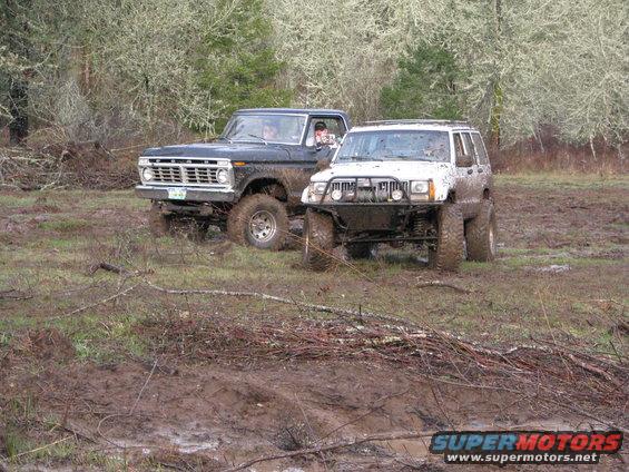 Black Ford F-Series truck and white Jeep Cherokee in mud. Truck has a 1975 grille