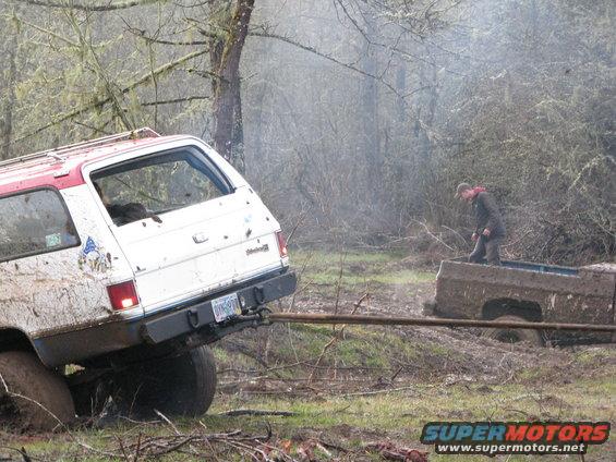 Rear view of white and red SUV stuck in mud, being towed by another vehicle