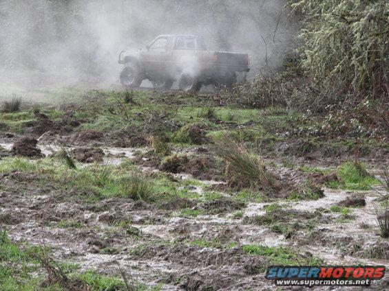 Pickup truck driving through a muddy, grassy area with smoke or steam coming from it