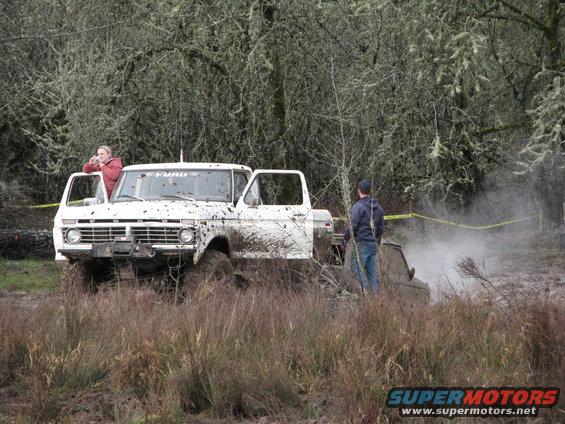 White 1975 Ford F-Series pickup truck stuck in mud, front view. Another vehicle is partially visible in the background