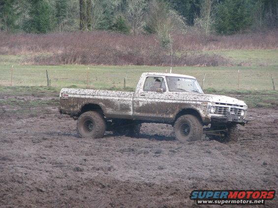 Muddy pickup truck driving through a muddy field. Looks like a 1975 Ford F-Series