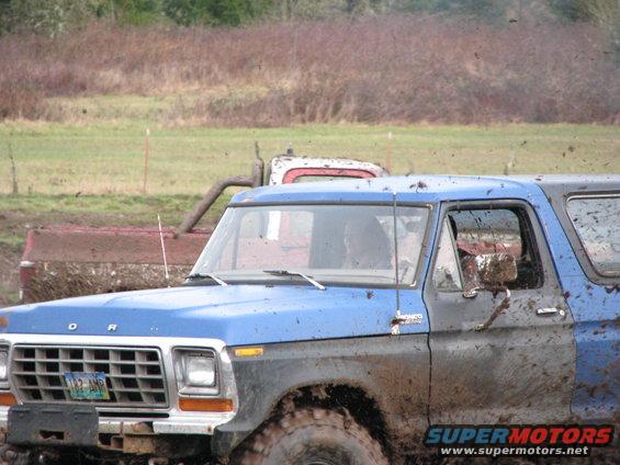 Muddy blue 1978 Ford Bronco front quarter view, with another red vehicle behind it