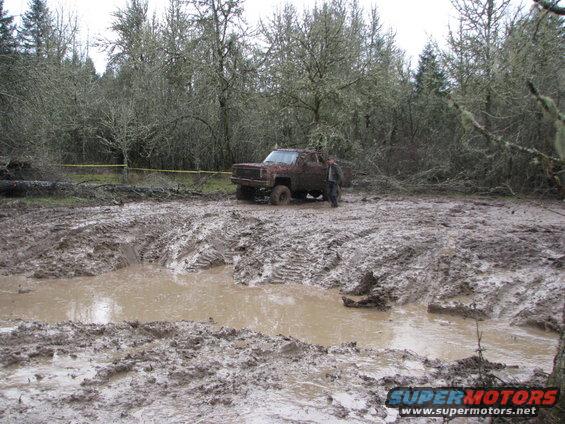 Off-road vehicle stuck in deep mud with trees in background