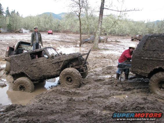 Off-road vehicles stuck in deep mud with people around them